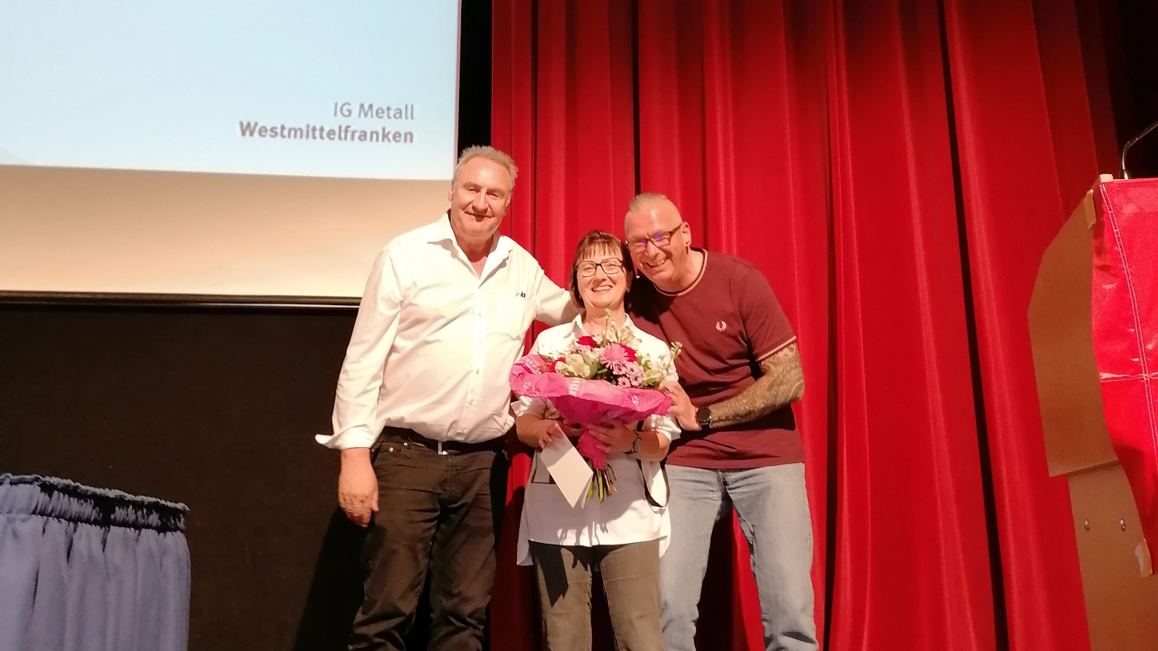 Der erste Bevollmächtigte Klaus-Dieter Winnerlein und Ortsvorstandsmitglied Steffen Salzer überreichen Kollegin Barbara März von der katholischen Betriebsseelsorge einen Blumenstrauß zum Geburtstag. Alle lächeln in die Kamera. 