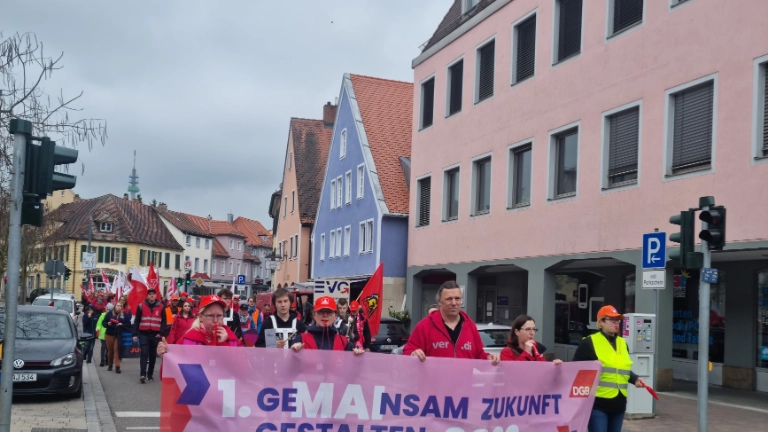 Gewerkschafter*innen laufen mit einem DGB Banner gemeinsam an der Spitze des Demozuges zum 1.Mai, hinter ihnen der restliche Demozug.