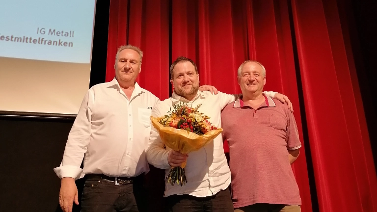 der erste Bevollmächtigte und ein Ortsvorstandsmitglied überreichen Jan Körper nach der Wahl einen Blumenstrauß 