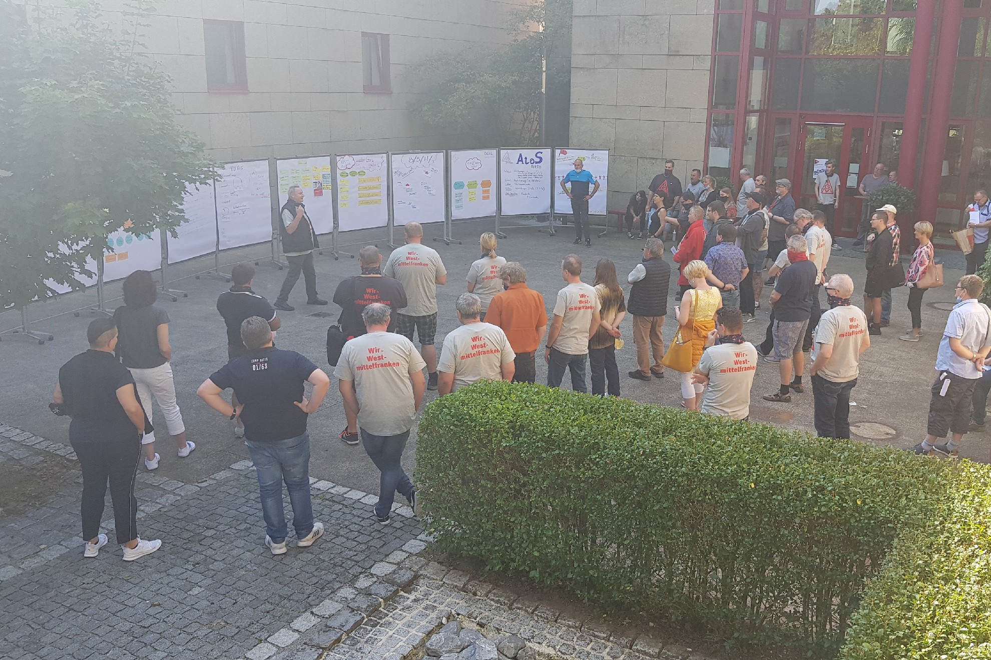 Menschen stehen im Innenhof der Bildungsst&auml;tte in Lohr am Main und h&ouml;ren einem Vortrag zu.